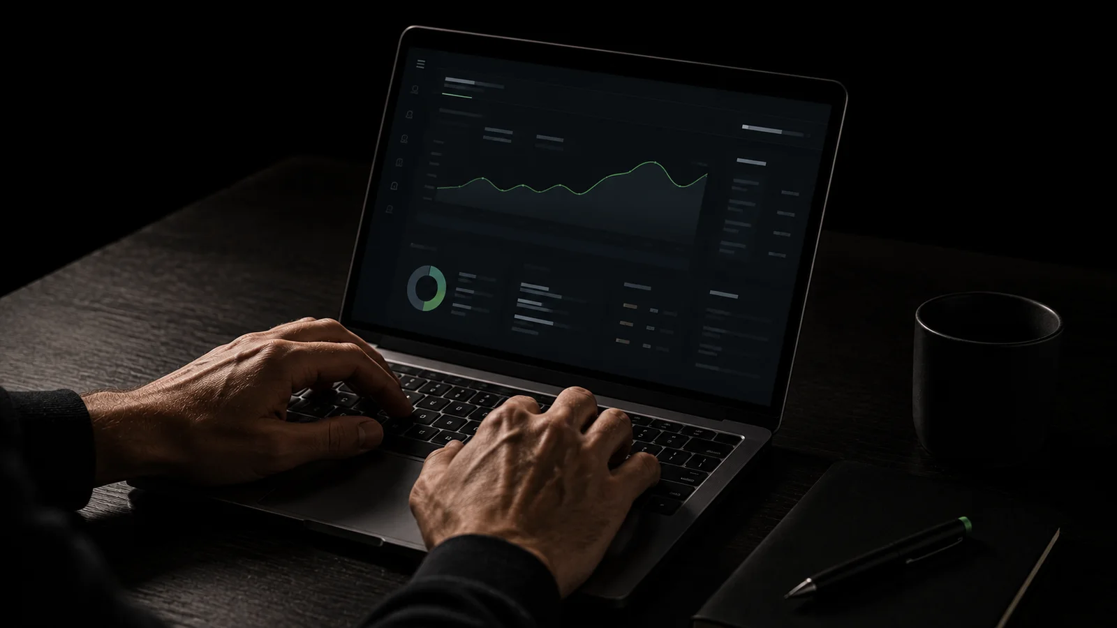 A pair of hands typing on a laptop displaying a weekly check-in dashboard with a green trend-line graph and progress charts, on a dark desk beside a notebook and pen