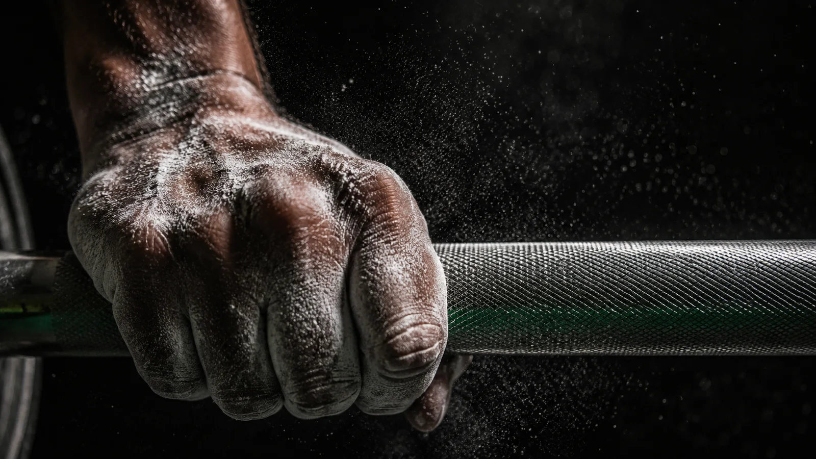 Close-up of a heavily chalked hand gripping a knurled barbell in dramatic low-key lighting, no face visible